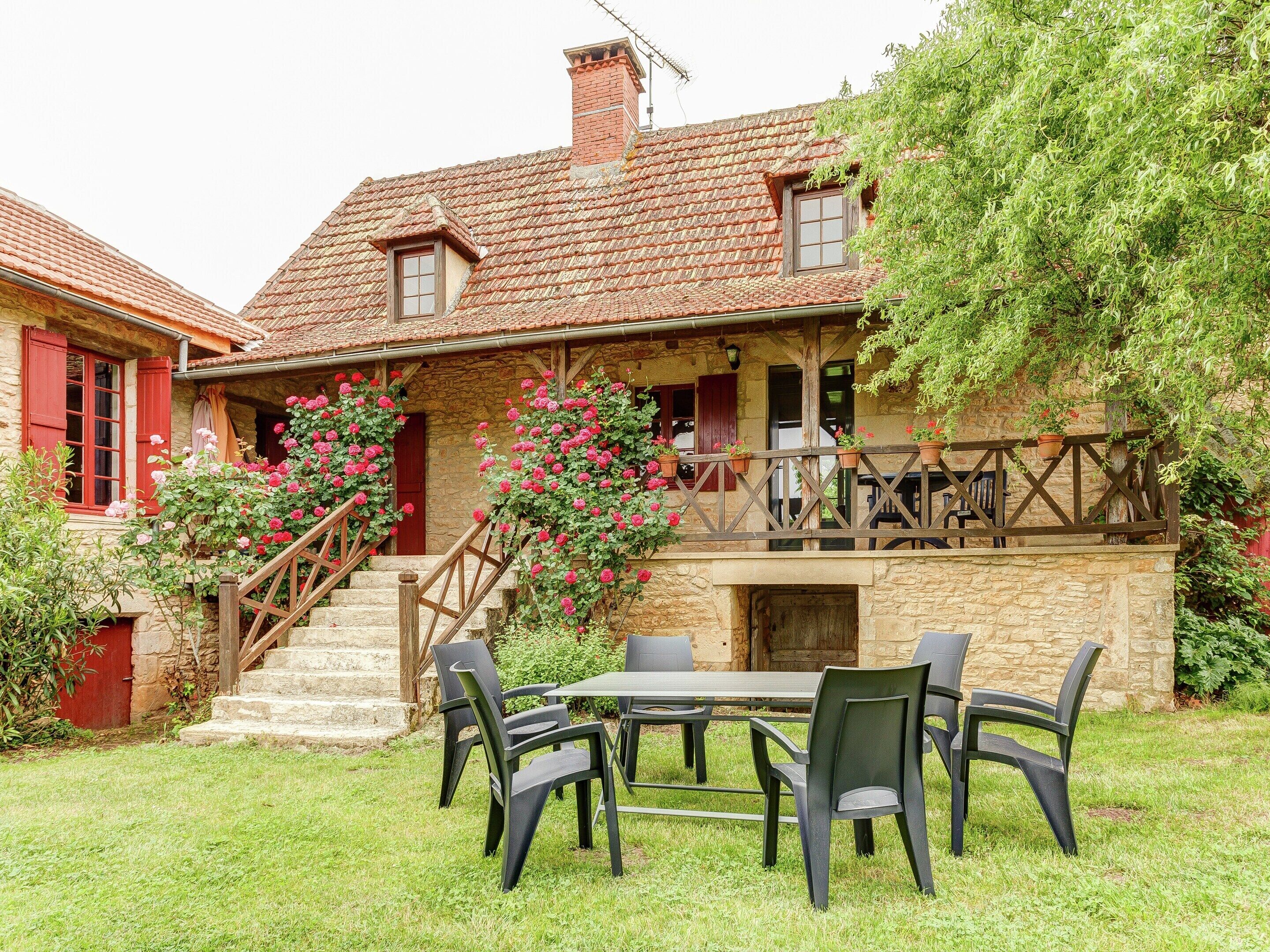 Una casa de piedra con un balcón de madera, una escalera que conduce a la entrada y un patio con mobiliario exterior.
