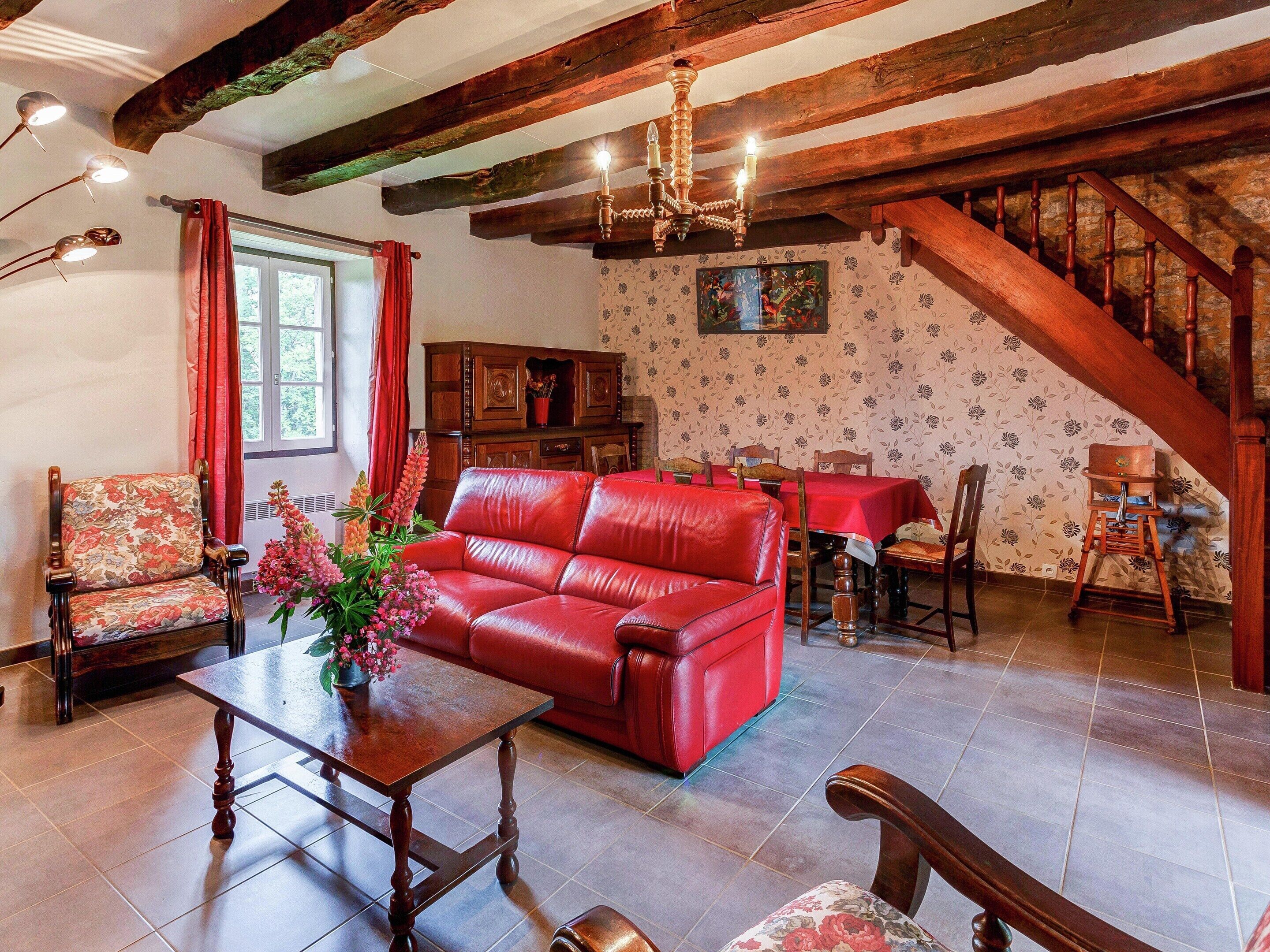 A room with a red leather sofa, wooden furniture, a chandelier, and a staircase.