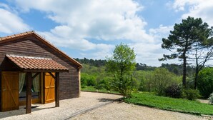A wooden cabin with a tiled roof, a gravel driveway, and a forested backdrop. - Blanquefort Nature Stay (Blanquefort-sur-Briolance)