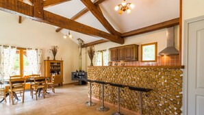 A spacious kitchen with wooden beams, a bar area, and a dining set. - Blanquefort Nature Stay (Blanquefort-sur-Briolance)