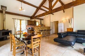 A spacious living area with a dining table, wooden chairs, a black leather sofa, and a kitchen with a stone backsplash. - Blanquefort Nature Stay (Blanquefort-sur-Briolance)