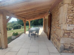 A covered patio with a stone wall, a table with chairs, and a view of the surrounding landscape. - Blanquefort Nature Stay (Blanquefort-sur-Briolance)