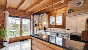 Una cocina con vigas de madera, una isla grande, armarios blancos y vistas a través de un ventanal corredero.