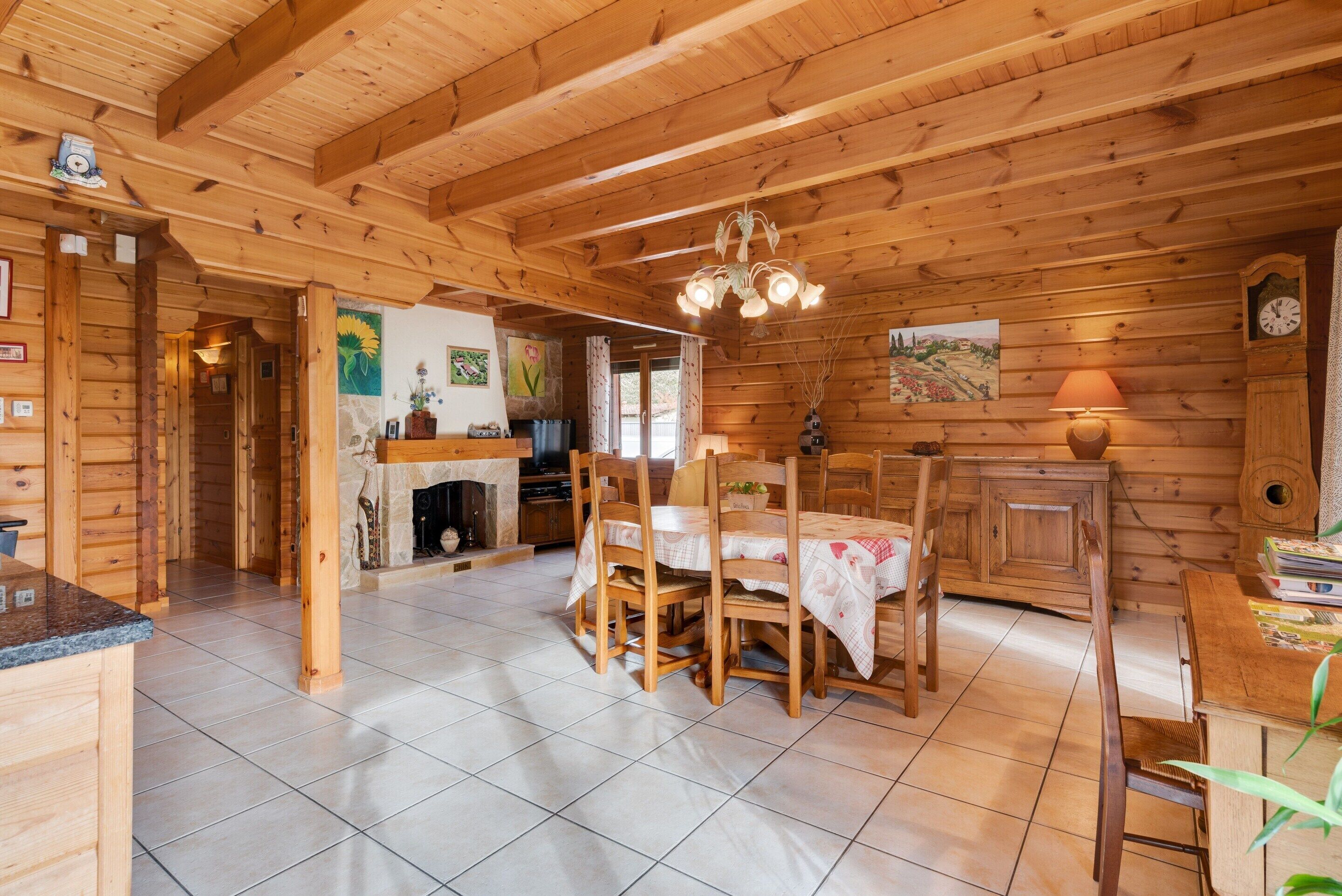 Interior de una cabaña de madera con comedor, chimenea y paredes de madera.