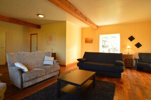 Un salon avec deux canapés, une table basse, un parquet et une fenêtre laissant entrer la lumière naturelle.