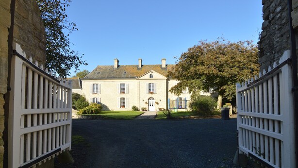 A large, historic building with a symmetrical facade, a central entrance, and a gravel driveway leading to a gated entrance. - Saint-clement Cottage Near the Sea (Osmanville)