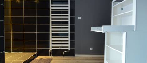 A modern bathroom with a white bathtub, a towel rack, and a built-in shelf unit.