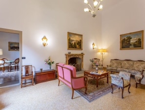 A traditional living room with a fireplace, a sofa, a pink chair, and a dining area with chairs and a table. - Villa in Mugello Hills With Private Pool (Vicchio)
