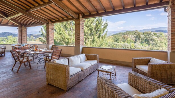 An open-air patio with wicker furniture, a dining table, and a view of the surrounding landscape. - Villa in Mugello Hills With Private Pool (Vicchio)