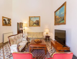 A living room with a sofa, armchairs, a coffee table, a TV, and paintings on the wall. - Villa in Mugello Hills With Private Pool (Vicchio)