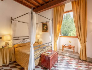 A room with a four-poster bed, a wooden nightstand, a small table with a lamp, and a window with curtains. - Villa in Mugello Hills With Private Pool (Vicchio)