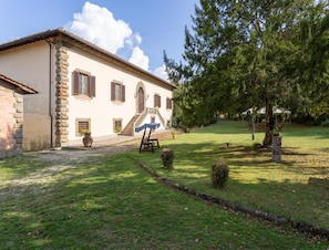 A two-story building with a stone facade, a covered staircase, and a well-maintained lawn with a tree and a swing set. - Villa in Mugello Hills With Private Pool (Vicchio)