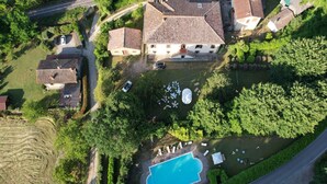 An aerial view of a residential area with a swimming pool surrounded by greenery, a road, and houses with tiled roofs. - Villa in Mugello Hills With Private Pool (Vicchio)
