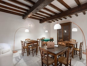 Un comedor con mesas y sillas de madera, una laptop sobre una mesa e iluminación colgante.