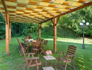 An outdoor wooden pergola with a table and chairs, surrounded by greenery. - Villa in Mugello Hills With Private Pool (Vicchio)