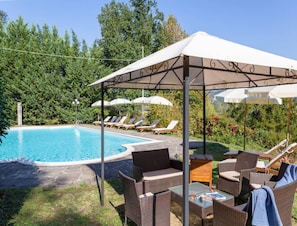 Un área junto a la piscina con sillones de descanso, una zona de estar techada y vistas despejadas a la piscina.