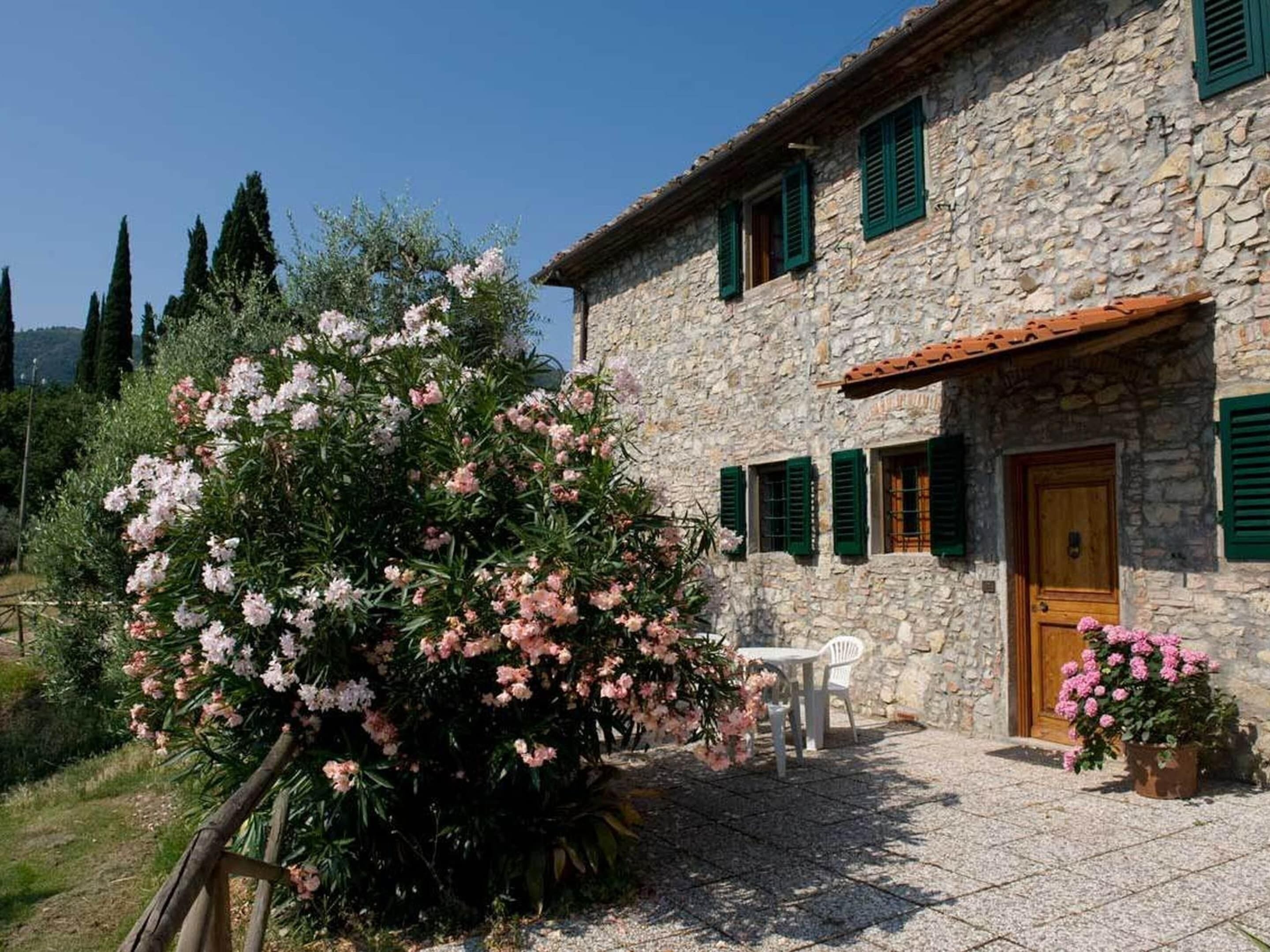 A stone building with a wooden door, green shutters, and a small outdoor seating area with a table and chairs.
