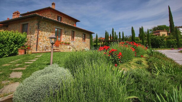 A stone house with a garden featuring red flowers and tall green grass. - Rustic Retreat With Pool (Lucignano)