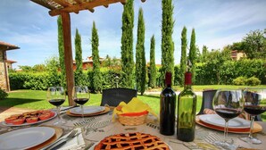 An outdoor dining setup with a table set for a meal, including plates, wine glasses, and a basket of fruit. - Rustic Retreat With Pool (Lucignano)