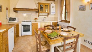 A kitchen with wooden cabinets, a microwave, an oven, and a dining table set for two with plates, glasses, and a bottle of wine. - Rustic Retreat With Pool (Lucignano)
