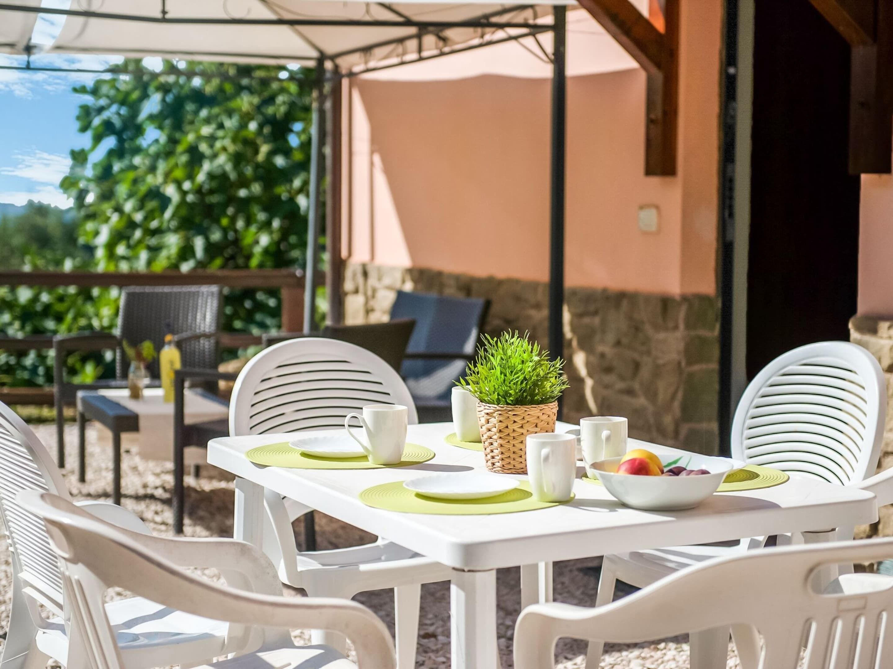 An outdoor patio with a table set for dining, surrounded by white chairs.