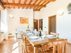A dining area with a wooden table set for six, surrounded by chairs. There is a painting on the wall, a door, and a window with curtains. - Agriturismo in the Appenines with Covered Swimming Pool & Hot Tub (Apecchio)