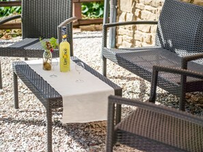 An outdoor seating area with wicker chairs and a table set with a bottle of Limone di Bergamo, a glass, and a small vase with flowers. - Agriturismo in the Appenines with Covered Swimming Pool & Hot Tub (Apecchio)
