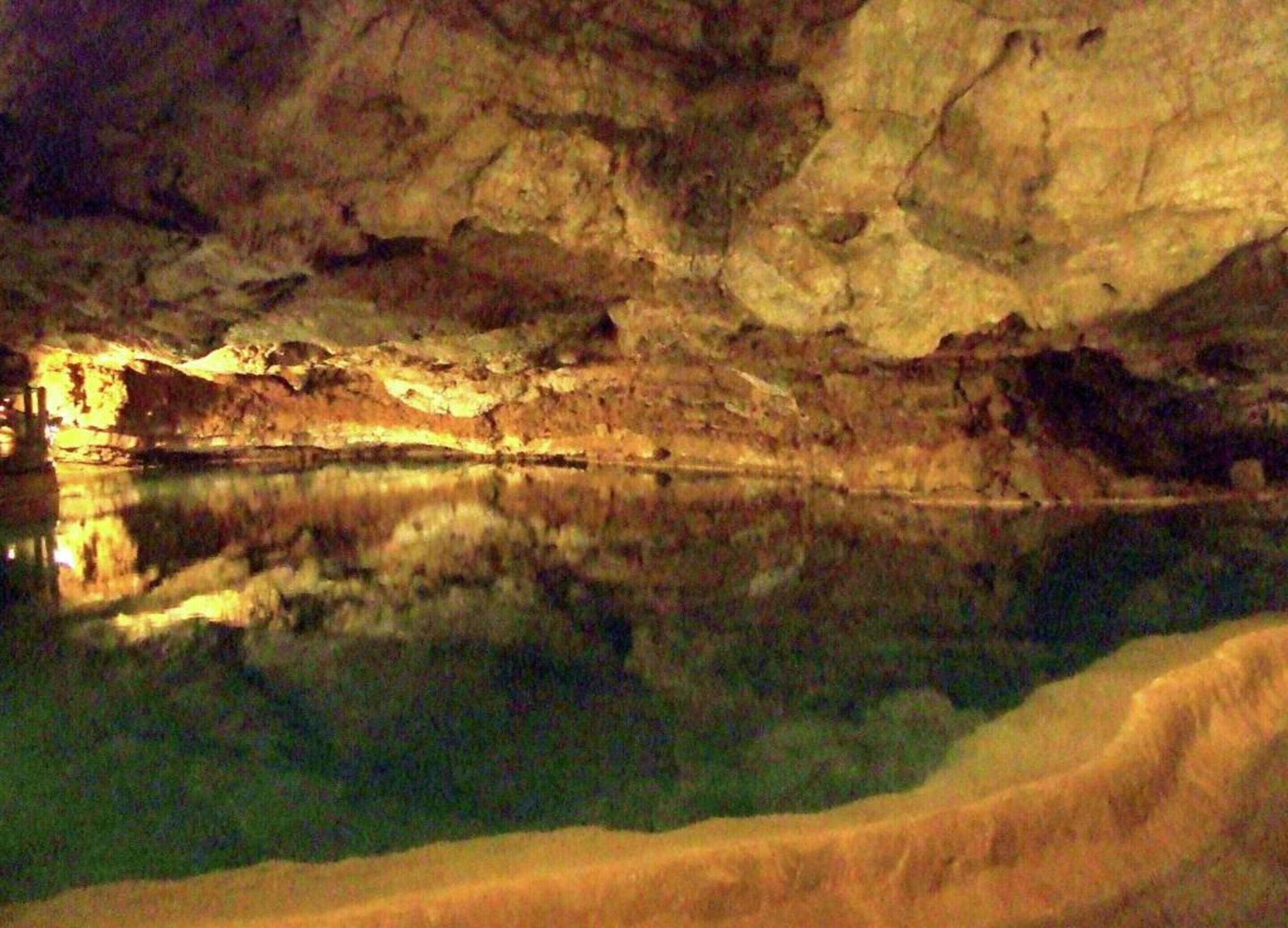 A cave interior with a reflective water surface and rocky walls.
