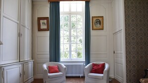 Et værelse med to hvide lænestole, en radiator, et vindue med blå gardiner, og tapet med mønster på den højre væg.