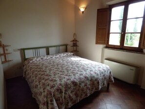 A bedroom with a bed, a window, a radiator, and a wall-mounted shelf. - Belvilla by OYO Fienile (Castelnuovo Berardenga)