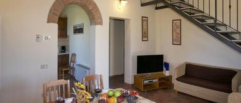 Comedor con una mesa para cuatro, un sofá, un mueble para la televisión y una escalera.
