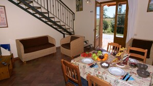 A dining area with a table set for four, surrounded by wooden chairs. A staircase is visible in the background, leading to an upper floor. - Belvilla by OYO Fienile (Castelnuovo Berardenga)