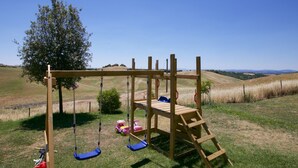 A wooden swing set with a bench and ladder, surrounded by a grassy field and a tree. - Belvilla by OYO Fienile (Castelnuovo Berardenga)