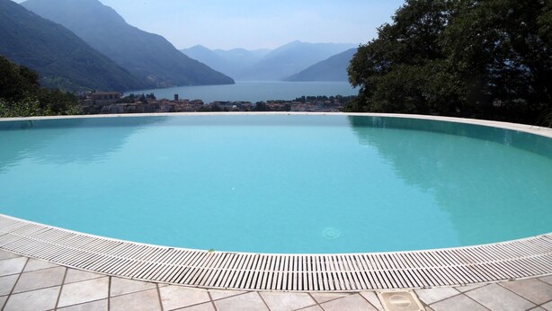 Ein klares, blaues Schwimmbecken mit Fliesen umgeben, umrahmt von Bergen und Bäumen.