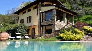 Ein zweigeschossiges Haus mit Steinverkleidung, einem Balkon und einem Pool davor.