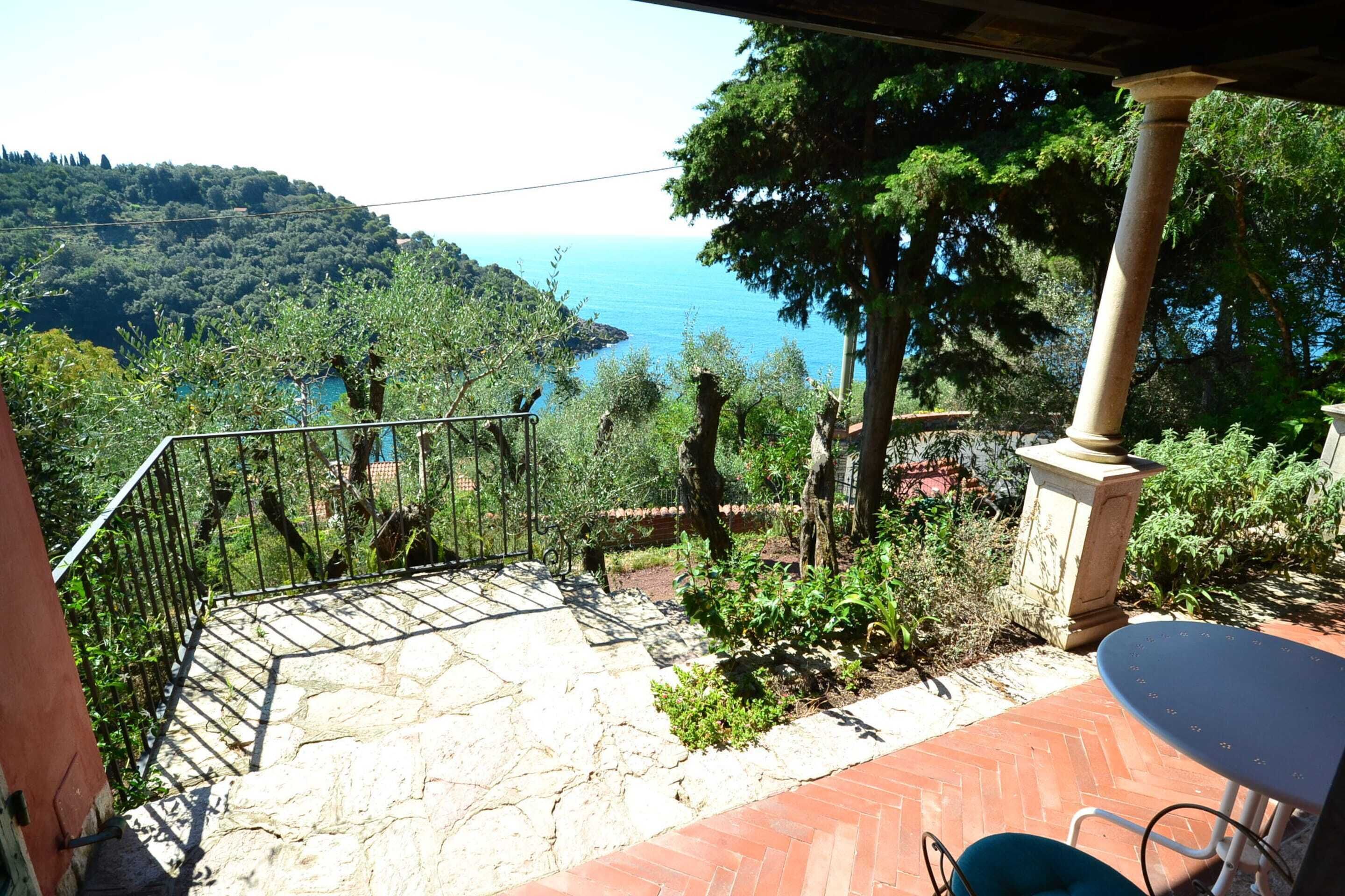 A stone staircase leading to a terrace with a view of the sea and hills.
