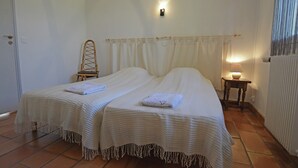 Quarto com duas camas, uma cadeira, mesa de cabeceira com abajur e radiador.
