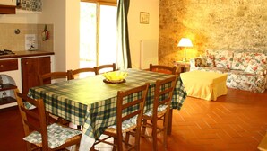A dining area with a table set for four, wooden chairs, a floral sofa, a lamp, and a kitchen area with a stove and counter. - Idyllic Tuscan Hideaway With Pool and spa (Sesto Fiorentino)
