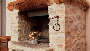 A rustic stone fireplace with a wooden mantel, a basket of firewood, and a metal ring attached to the wall. - Idyllic Tuscan Hideaway With Pool and spa (Sesto Fiorentino)