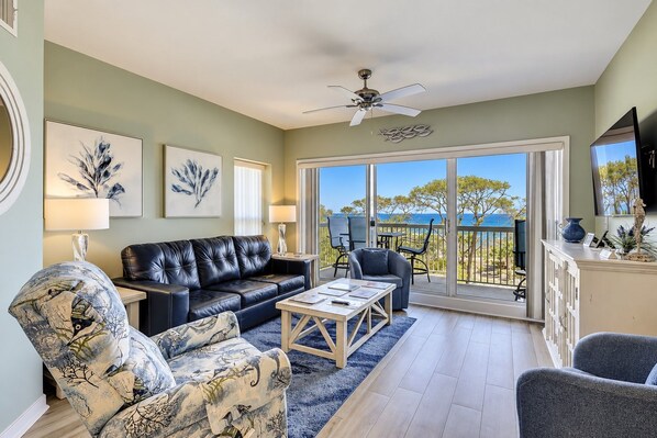 A living room with a leather sofa, patterned armchairs, a coffee table, and a balcony with a view.
