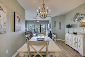 A dining area with a chandelier, wooden table, chairs, and a view through a glass door.
