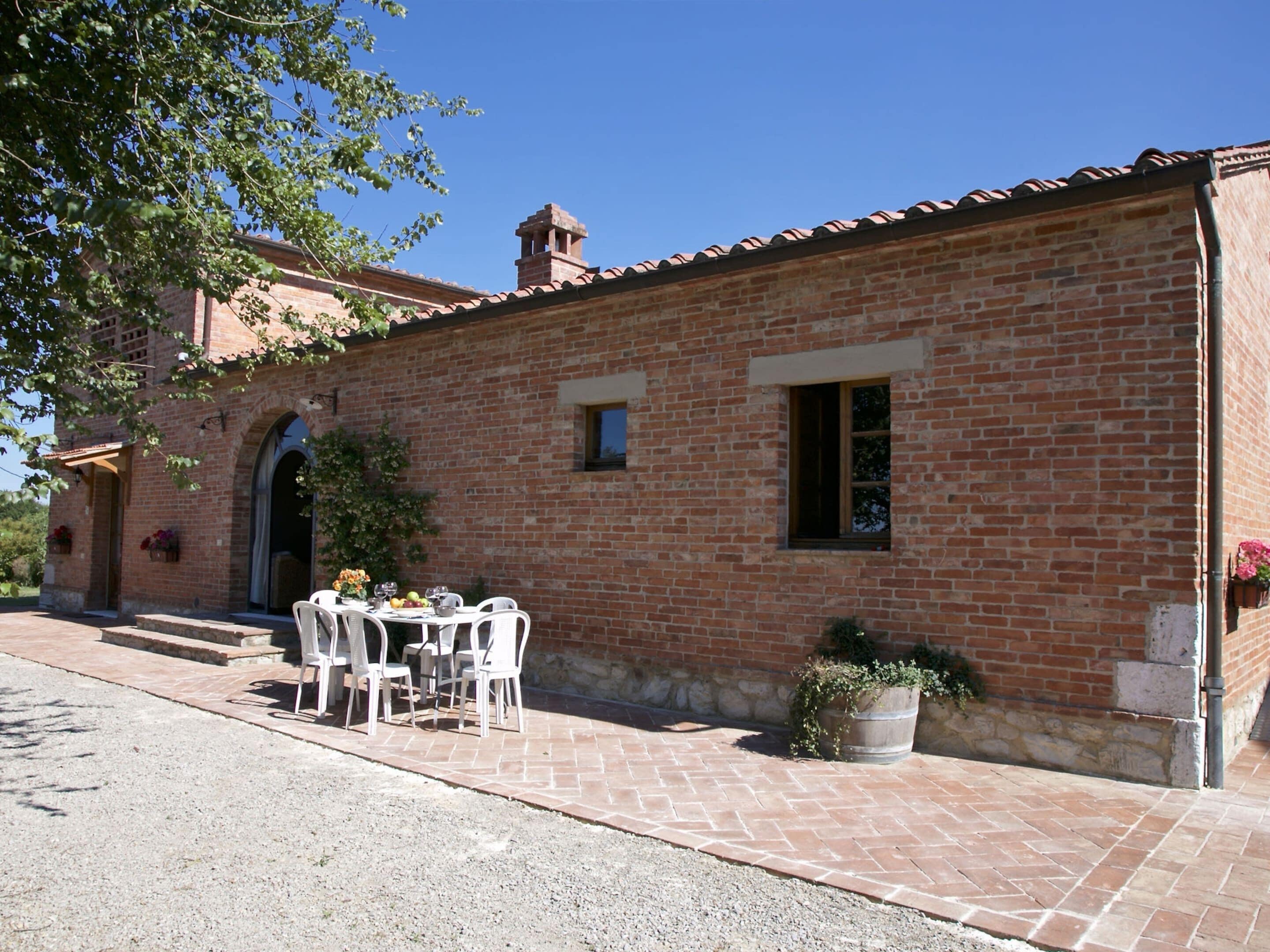 A brick building with a tiled roof, a small window, and a door. There is a table with chairs outside.
