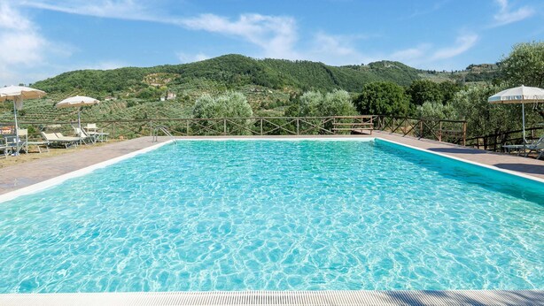 A swimming pool with clear blue water, surrounded by lounge chairs and umbrellas, set against a backdrop of green hills and a clear sky. - Farmhouse Abode With Pool and Tuscan Charm (Quarrata)