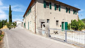 A two-story stone building with green shutters, a gated entrance, and a clear road leading to it. - Farmhouse Abode With Pool and Tuscan Charm (Quarrata)