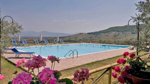 Ein Swimmingpool mit blauen Liegestühlen und einer Hügelkulisse im Hintergrund.