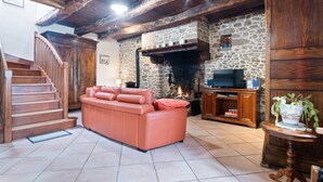 A living room with a stone fireplace, wooden staircase, and a television on a wooden stand. - Charming Child-friendly Holiday Home (La Boussac)