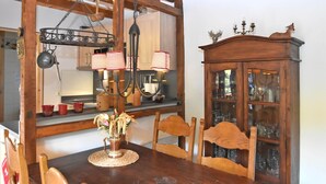 Una mesa de comedor de madera con sillas, una araña y un aparador con puertas de cristal.