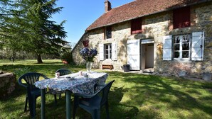 A stone house with a tiled roof, a table with chairs, and a large tree in the yard. - Holiday Home in Decize Near Beach (Flaine)