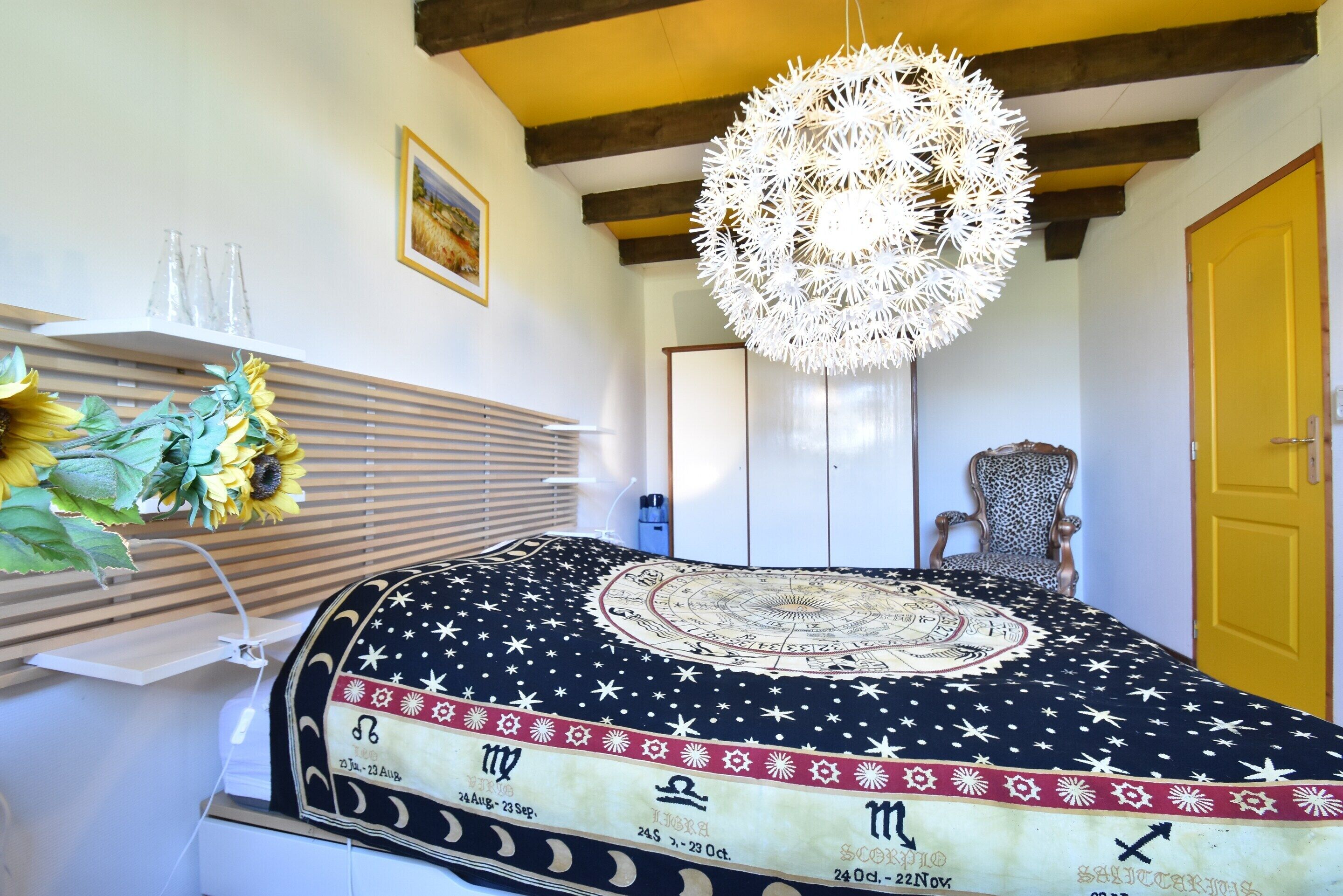 A room with a bed featuring a starry night design, a hanging light fixture, a chair, and a door.