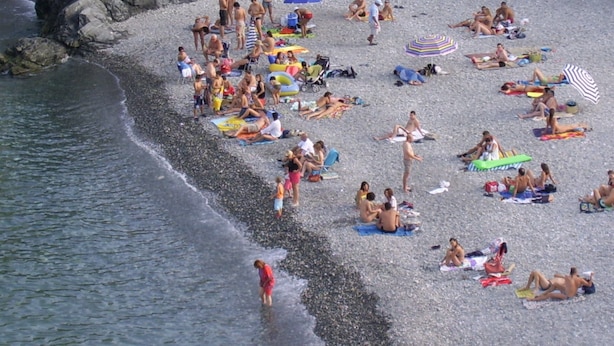 Una playa concurrida, gente tomando el sol y nadando.